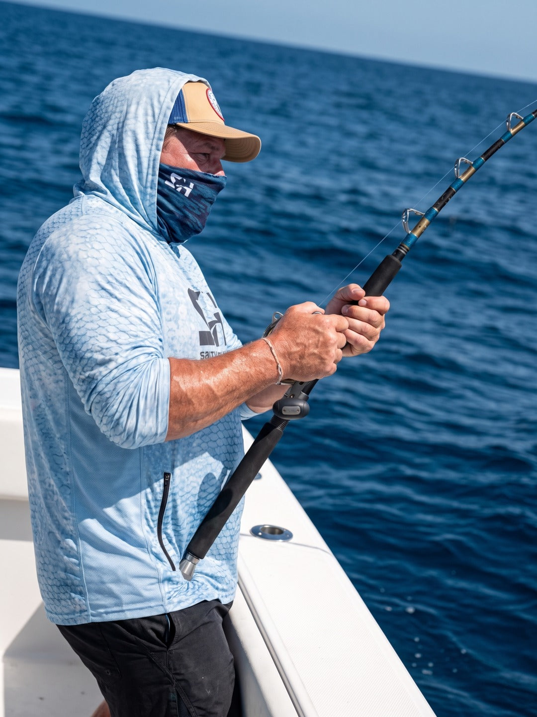 Angler in the Fish Scale Solar Vent hoodie fighting a fish offshore with a face wrap pulled up
