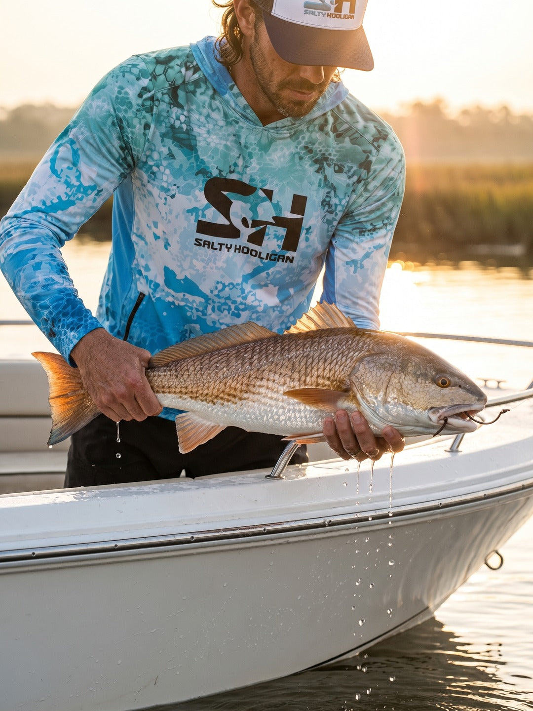 Angler in the Ocean Pro Tech Hoodie lifting a redfish over the side of a skiff at sunset