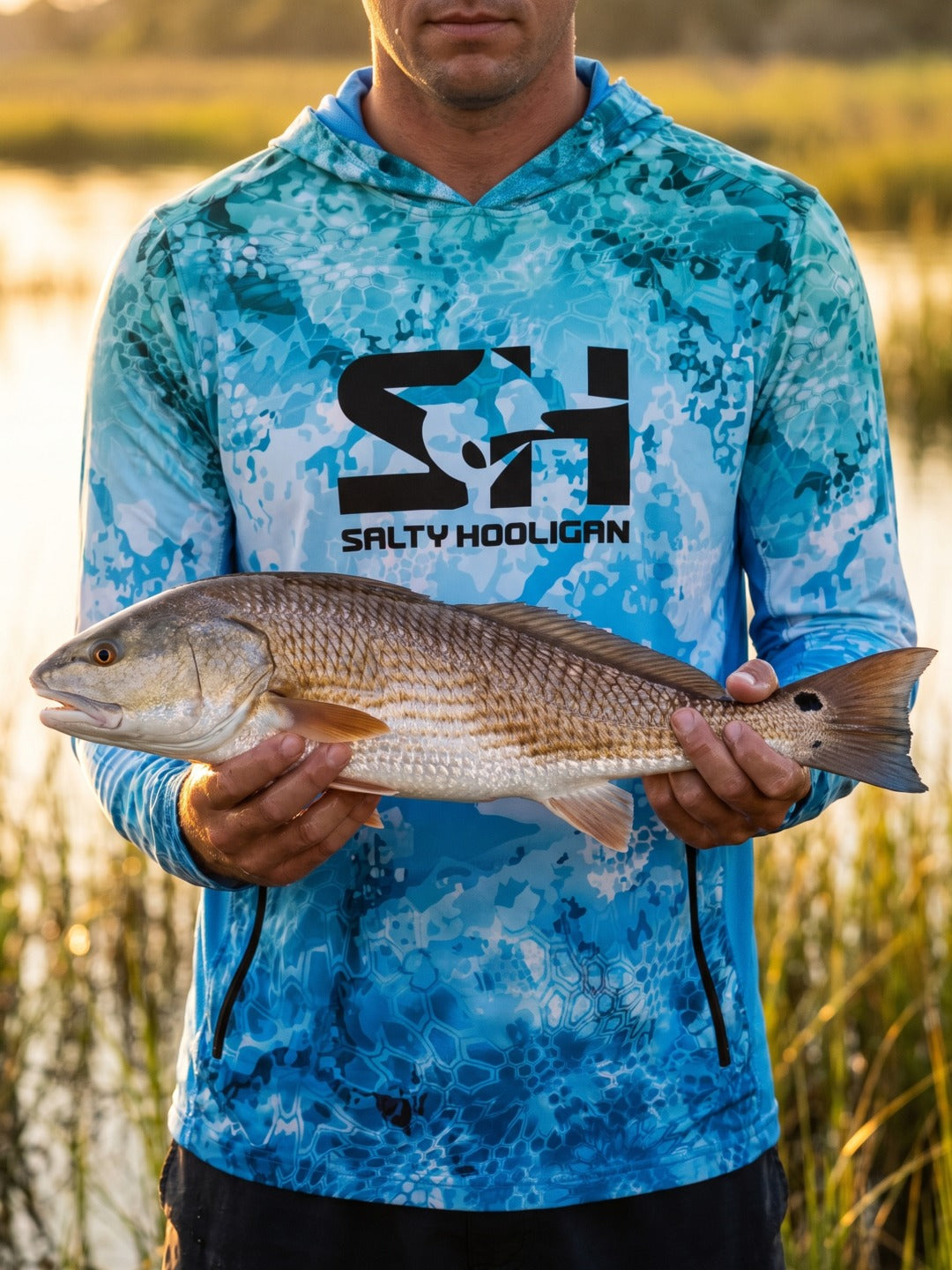 Angler in the Ocean Pro Tech Hoodie holding a redfish in front of marsh grass