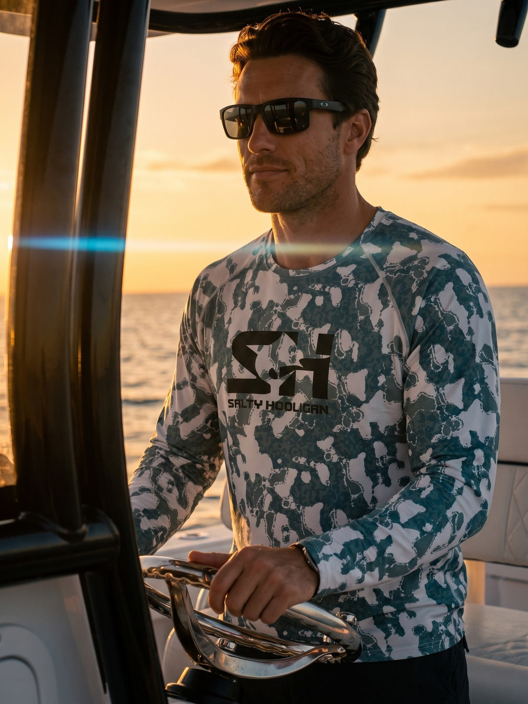 Man at the helm of a boat at sunset wearing the Riptide Performance long sleeve